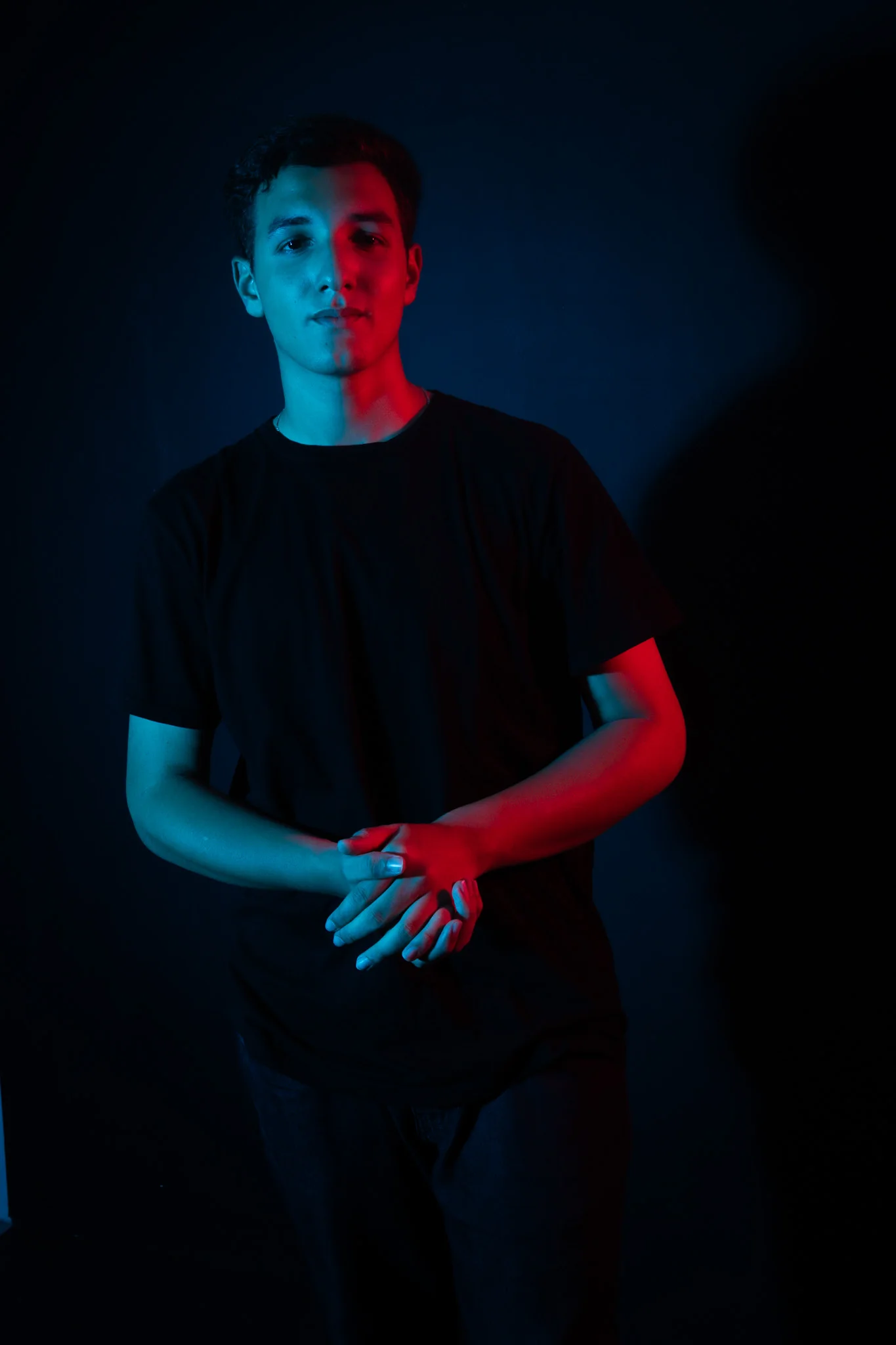 Vinicius com as mãos unidas sob iluminação azul e vermelha